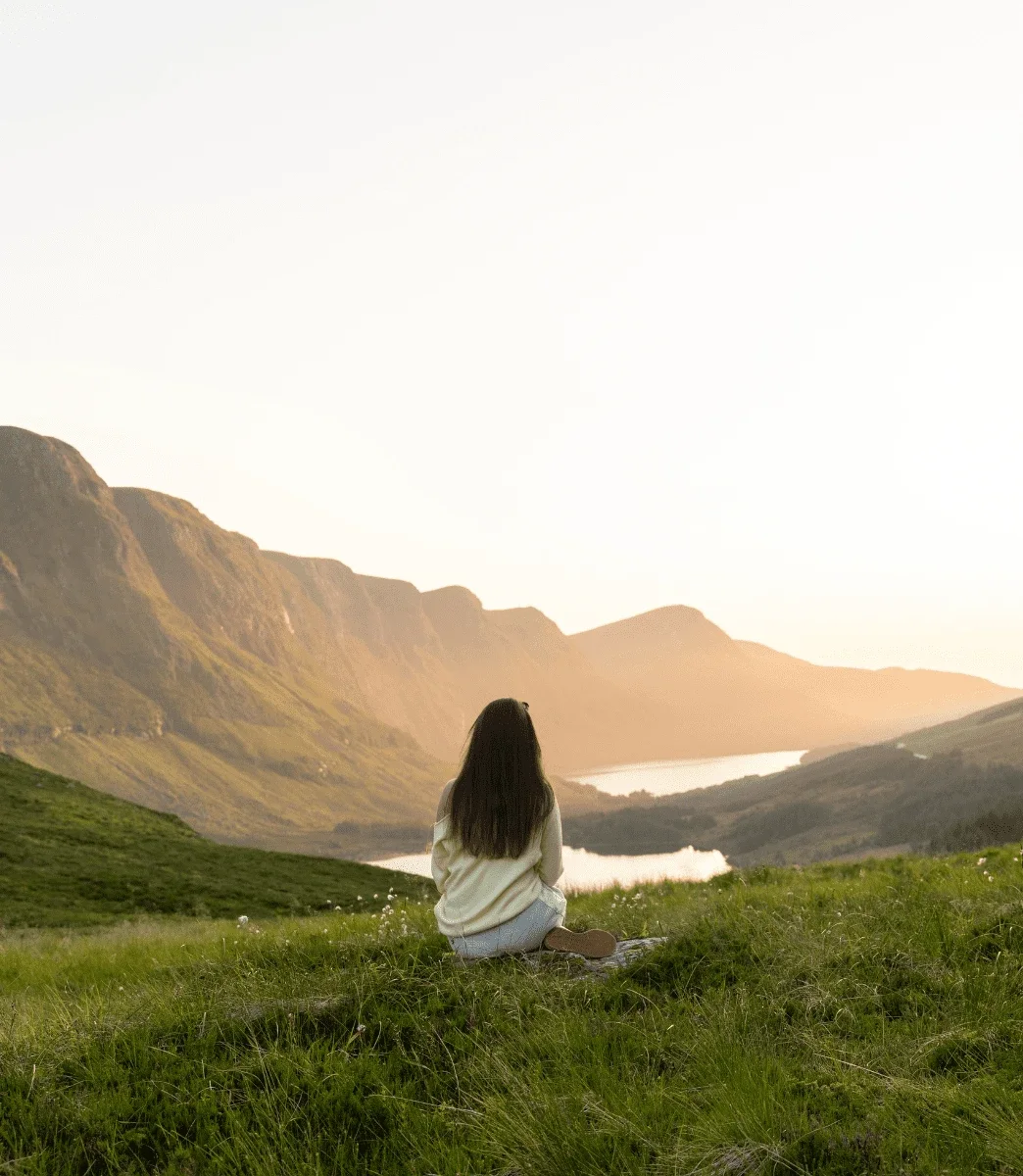Gjest sitter i lyngen og ser utover fjord og fjell på Stad i kveldssol