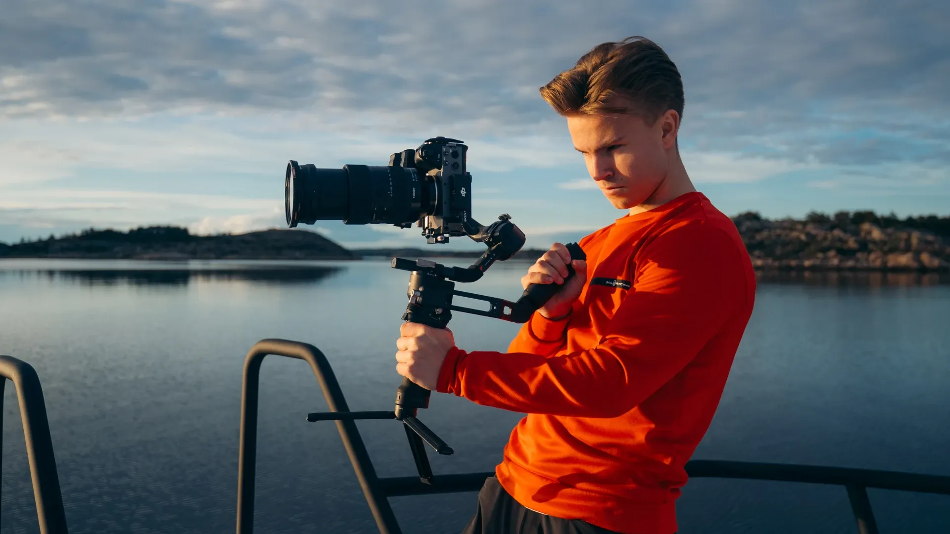 Videograf i oransje genser filmer fra båtdekk i kveldssol