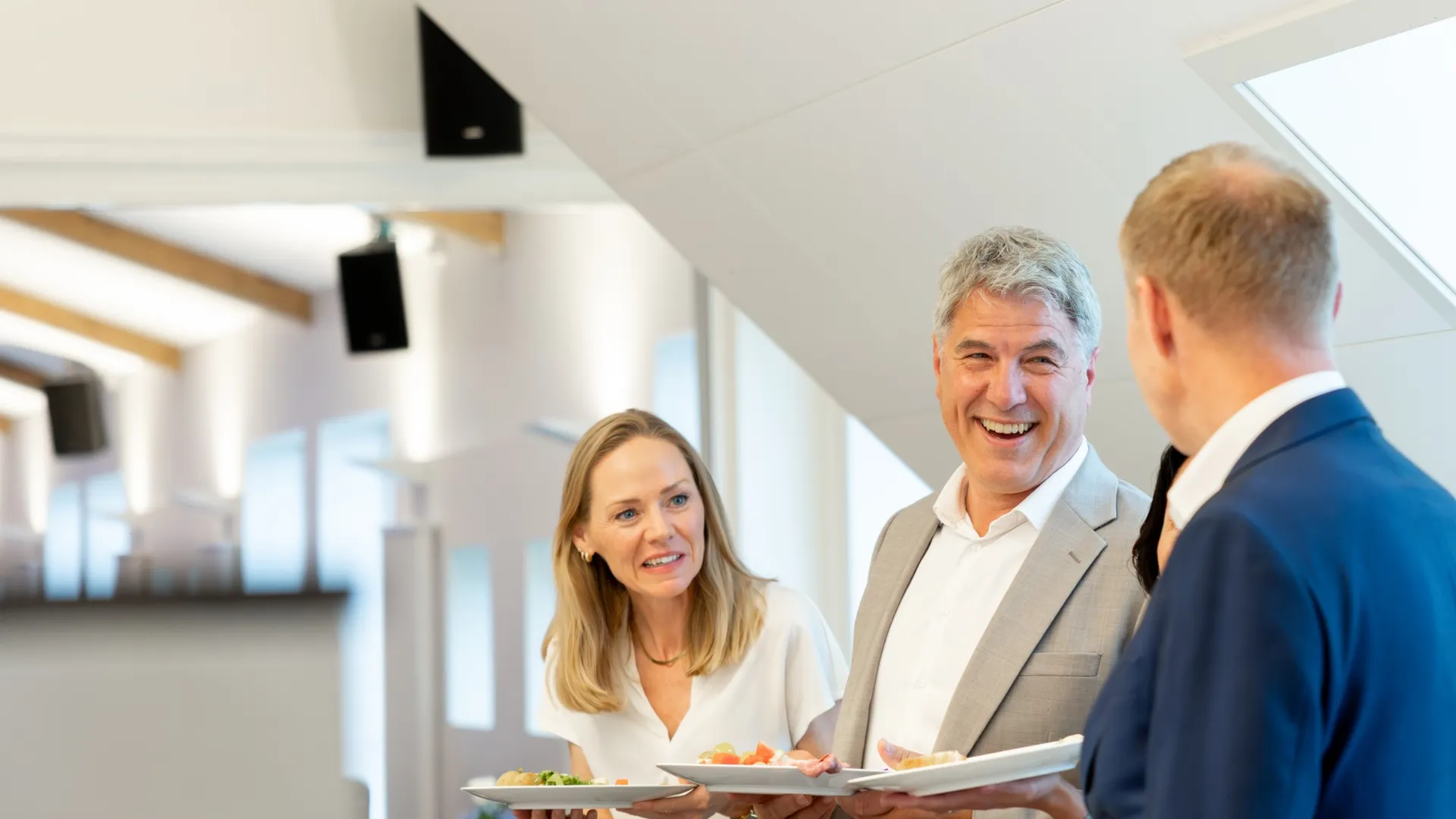 Gjester i godt humør med tallerkener i et lyst selskapslokale